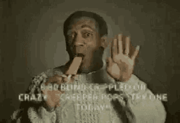 a man in a sweater is eating a popsicle and making a funny face .