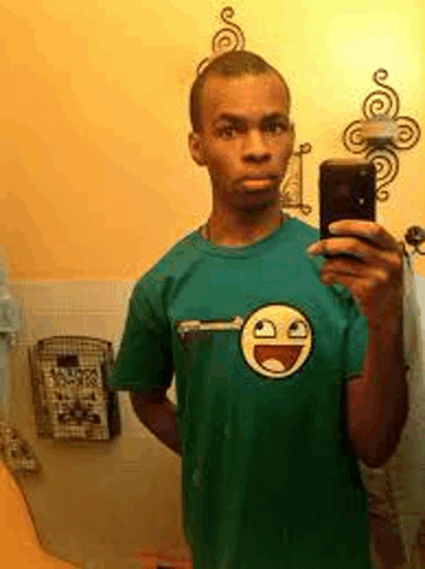 a man in a green shirt is taking a selfie in a bathroom with his phone .