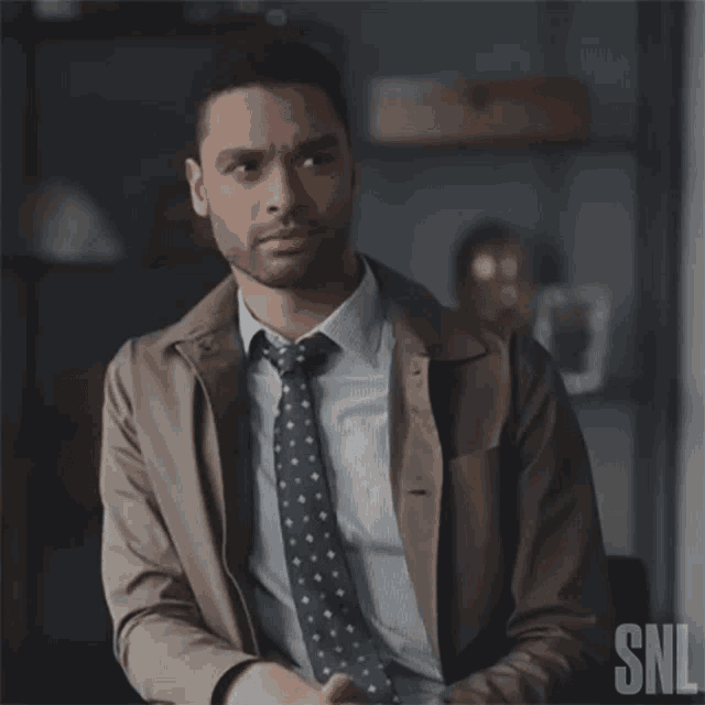 a man in a suit and tie is sitting in front of a snl logo .