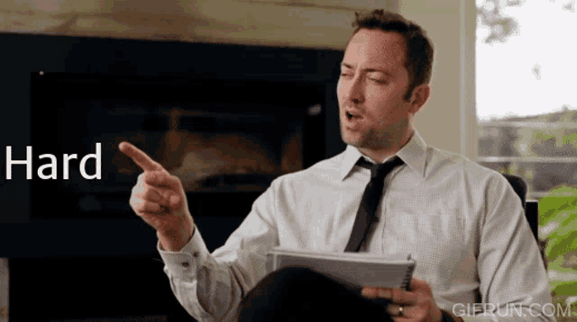 a man in a white shirt and tie is pointing at the word hard while holding a tablet