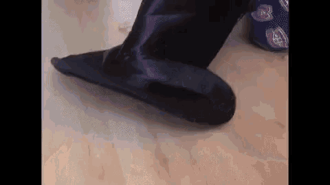 a person wearing black slippers is standing on a wooden floor .