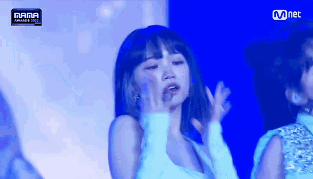 a woman in a white dress is dancing on a stage with a mnet logo in the background