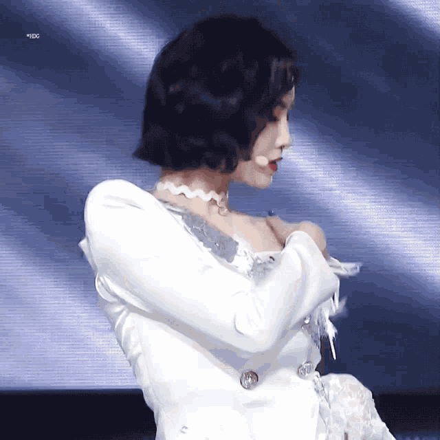 a woman wearing a white dress and a choker looks down at something