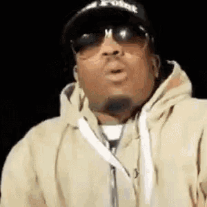 a man wearing sunglasses , a hat and a hoodie is blowing a kiss .