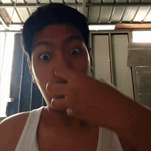 a man in a white tank top is covering his nose