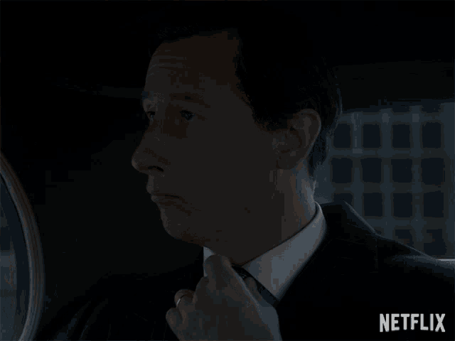 a man in a suit and tie is sitting in a car with a netflix logo behind him