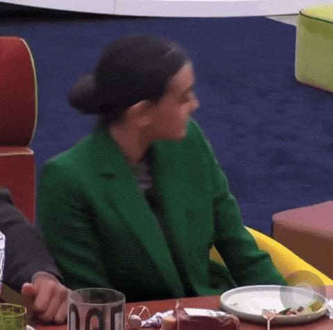 a woman in a green jacket sits at a table with plates of food