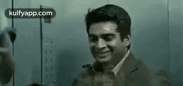 a man in a suit is smiling in an elevator while talking on a cell phone .
