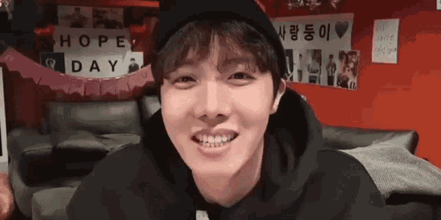 a young man wearing a black hat and a black hoodie is smiling and looking at the camera .