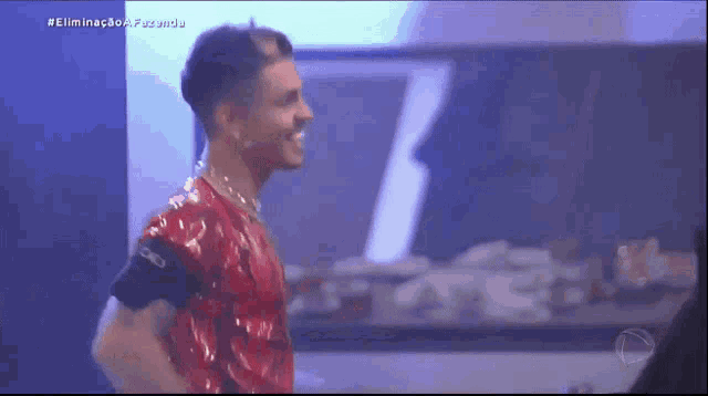 a man in a red shirt is smiling in front of a sign that says eliminacao