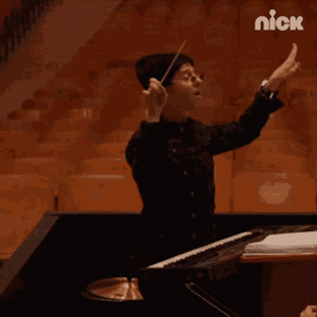 a man playing a piano in an auditorium with the nick logo on the bottom right