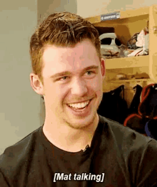 a man is smiling and talking in a locker room while wearing a black shirt .