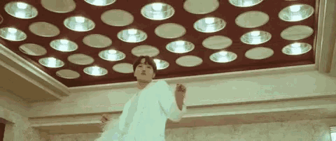 a man in a white jacket is standing in front of a ceiling with circles of lights