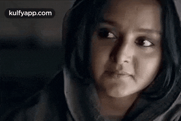a close up of a woman 's face with a hood on her head and a sad look on her face .