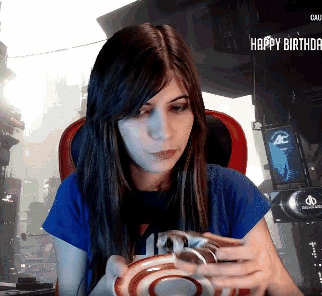 a woman in a blue shirt is holding a cup and saucer in front of a screen that says " happy birthday "