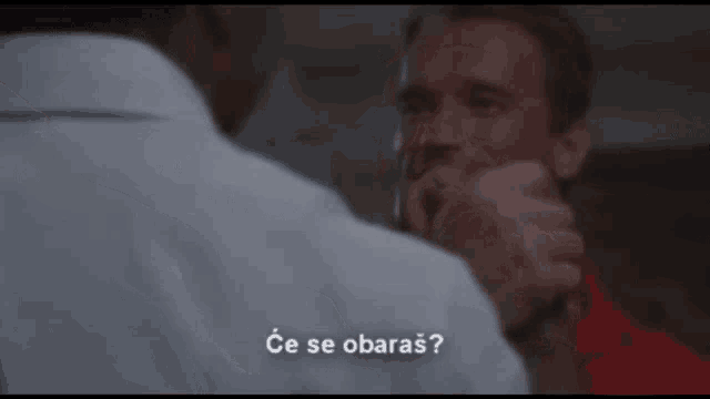 a man in a white shirt is talking to another man in a red shirt in a scene from a movie .