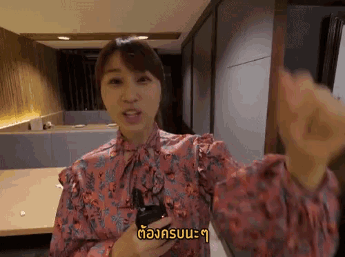 a woman in a pink floral shirt is holding a cell phone with a yellow sticker on it that says ' a '