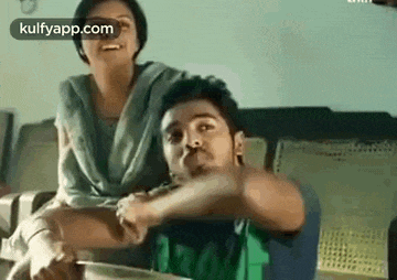 a man and a woman are sitting on a couch . the man is holding the woman 's arm .