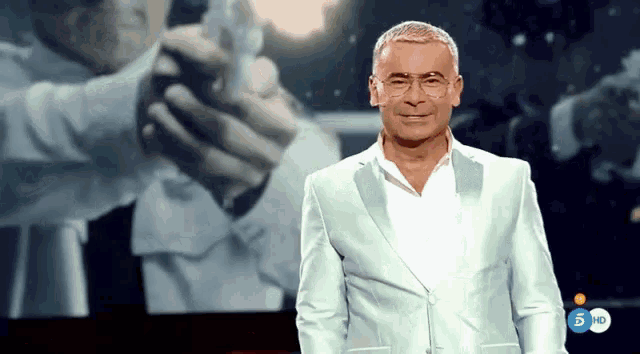 a man in a white suit is standing in front of a screen that says 5 10