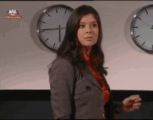 a woman stands in front of a wall of clocks with one that says internacional on it