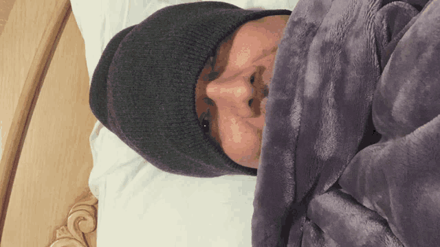 a man wearing a beanie is laying on a bed with a purple blanket