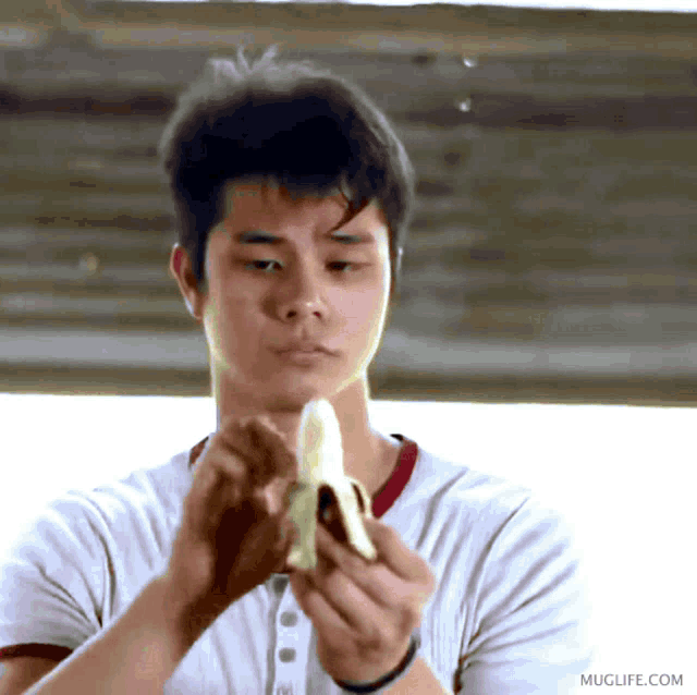a man in a white shirt is peeling a banana and muglife.com is visible in the corner