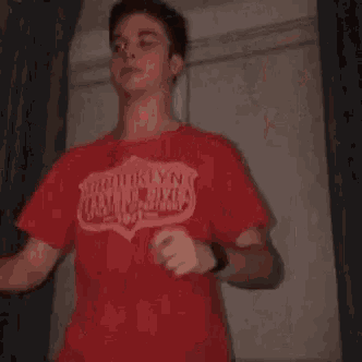 a young man in a red shirt is dancing in a room with his arms outstretched .