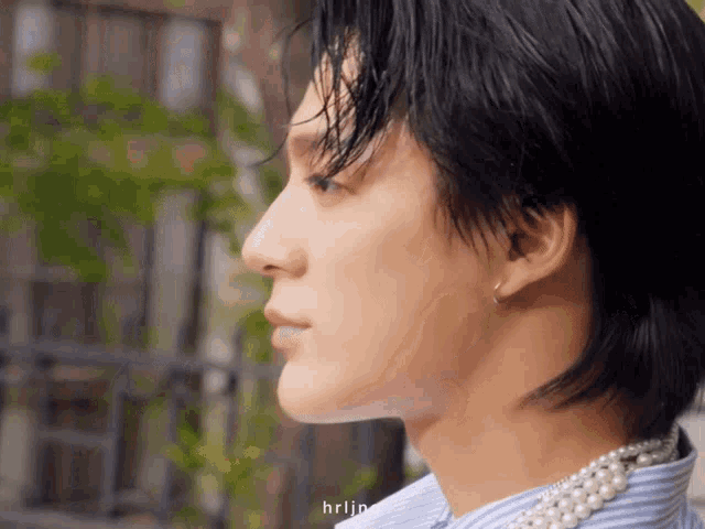 a close up of a man 's face with a pearl necklace on his neck