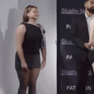 a woman in a black dress is standing next to a man in a suit in front of a sign that says slushy