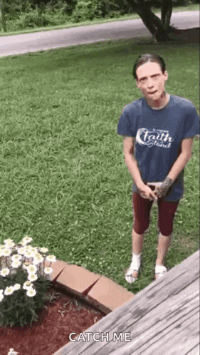 a man in a blue shirt is standing in front of a flower bed in a yard .