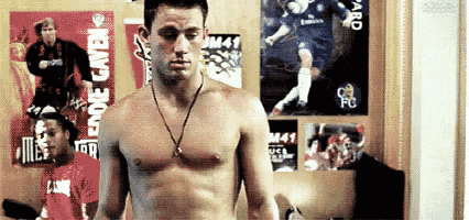 a shirtless man is standing in front of a wall with posters of soccer players .