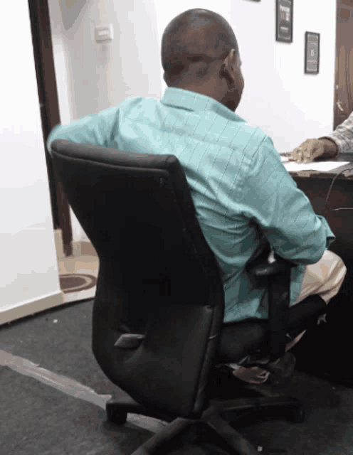 a man in a blue shirt is sitting in a black chair