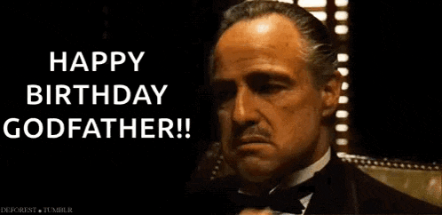 a man in a tuxedo is sitting in front of a window and says `` happy birthday godfather '' .