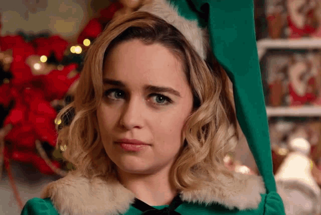 a woman in a green elf costume looks at the camera with a sad look on her face