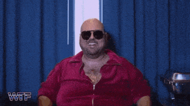 a bald man wearing sunglasses and a red jacket is smiling