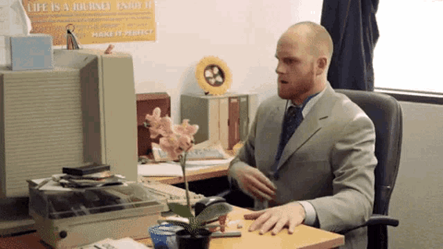 a man in a suit sits at a desk in front of a poster that says life is a journey enjoy it