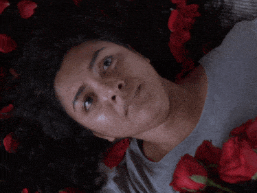 a woman is laying on a bed surrounded by red roses and petals