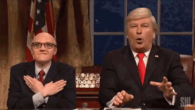 two men sitting at a desk with the letters snl on the bottom left