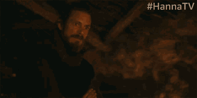 a man with a beard is standing in a dark room with the hashtag #hannatv above him