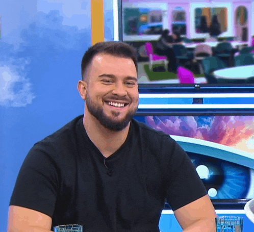 a man with a beard is smiling in front of a tv screen