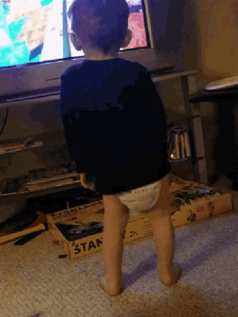 a baby standing in front of a stanley box