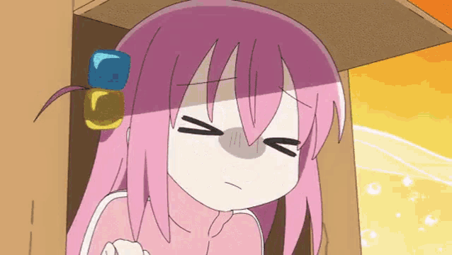 a cartoon girl with pink hair is sitting under a table with her eyes closed and a blue cube on her head .
