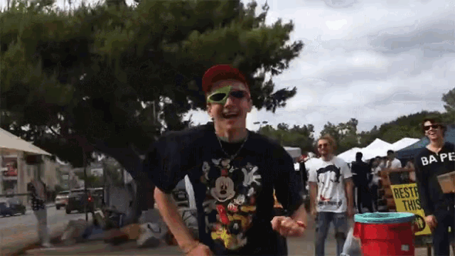 a man wearing sunglasses and a mickey mouse shirt stands in front of a sign that says restore this