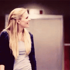 a woman with blonde hair is wearing a blue jacket and a grey shirt .