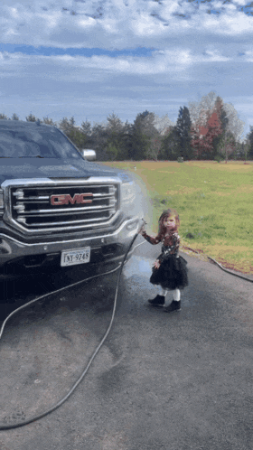 a little girl stands in front of a gmc truck