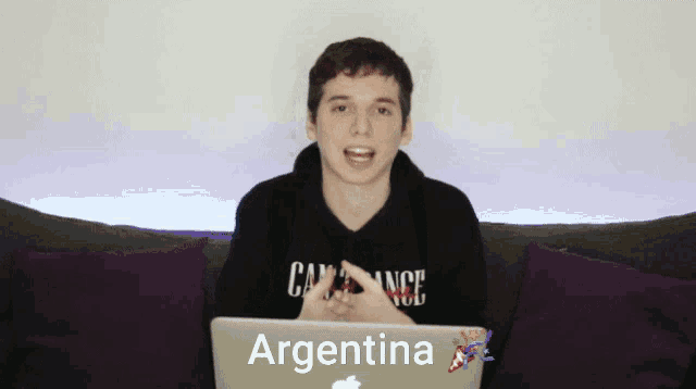 a young man sitting on a couch with a laptop that says argentina on it