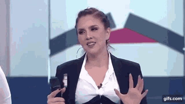 a woman in a black suit and white shirt is talking into a microphone on a television show .