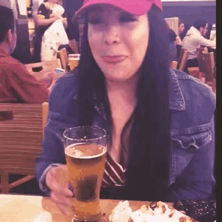 a woman is sitting at a table holding a glass of beer