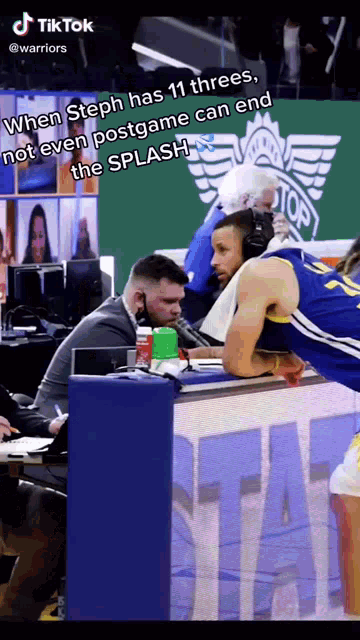 a basketball player is leaning on a bench and talking into a microphone while a man in a suit looks on
