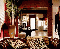a woman is walking through a living room with a couch and a plant